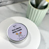 A small round tin of brush cleaner sits on a white round tray. The lid is light lavender with black text reading 'SOLID MAKEUP BRUSH CLEANER' and a small brush-and-tube illustration.