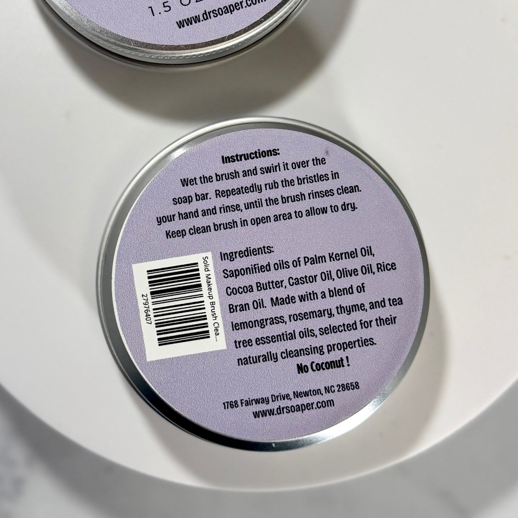 Close-up of the bottom of a round metal tin showing product instructions, ingredients, a barcode, and the website www.drsaper.