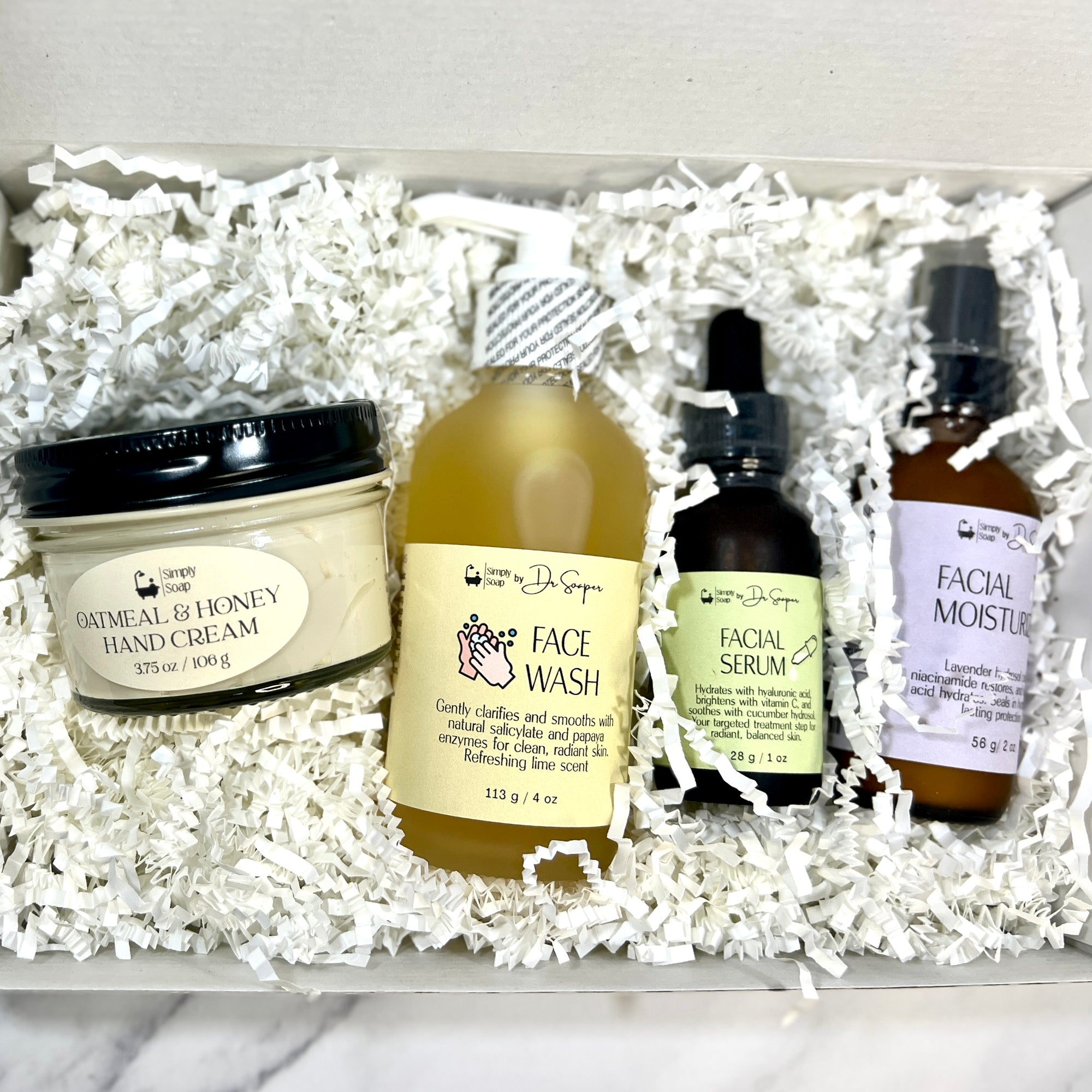 Set of skincare products including hand cream, face wash, facial serum, and facial moisturizer in a box.