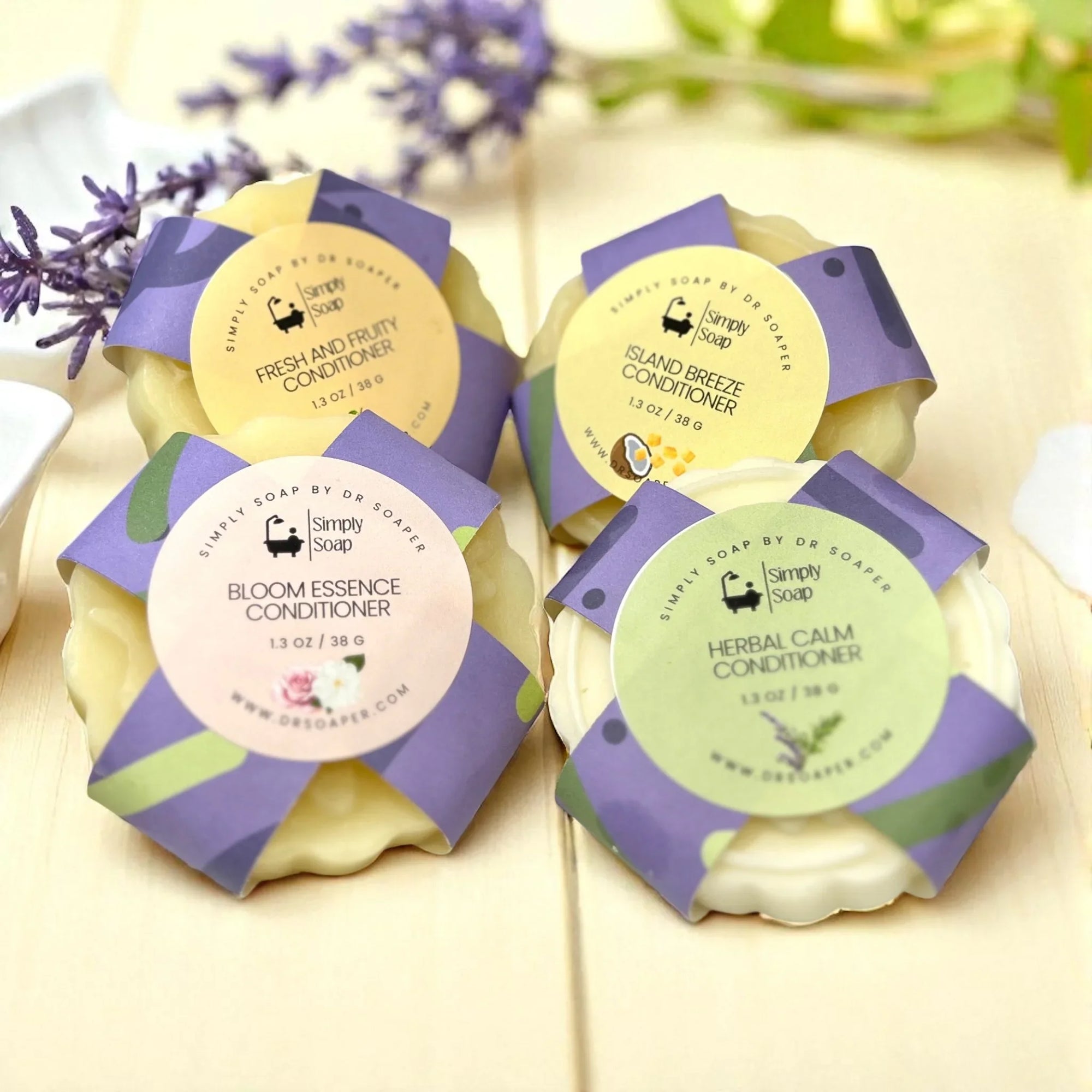 Four Simply Soap Solid conditioner bars with labels on a light  wood background with lavender flowers.