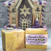 Two bars of soap with a decorative gingerbread house in the background