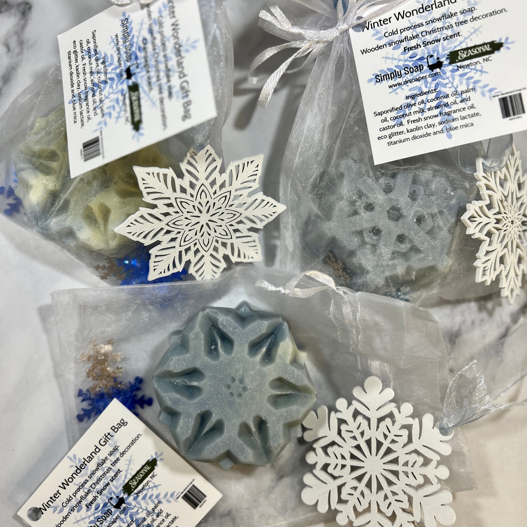 Snowflake-shaped soap bars in clear bags with decorative snowflakes on a light background